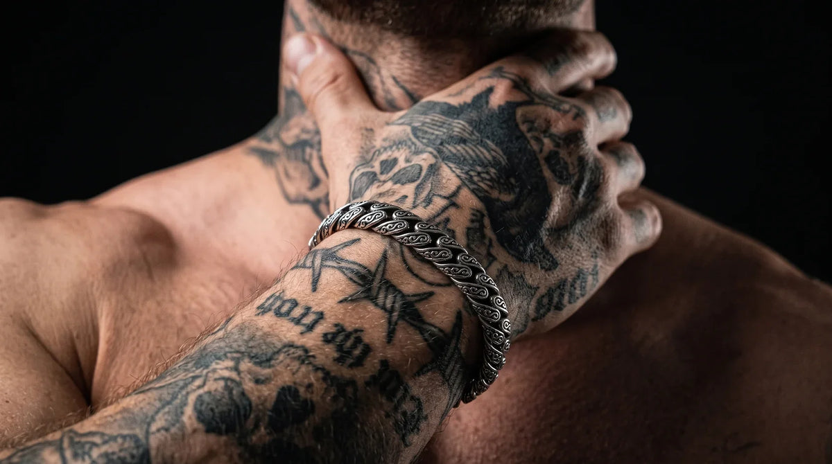 Tattooed man wearing a detailed stainless steel Viking bracelet on his wrist against a dark background