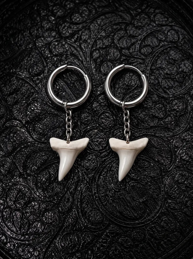 Abyss Fang shark tooth earrings with one white tooth beneath each silver-tone hoop on black patterned fabric