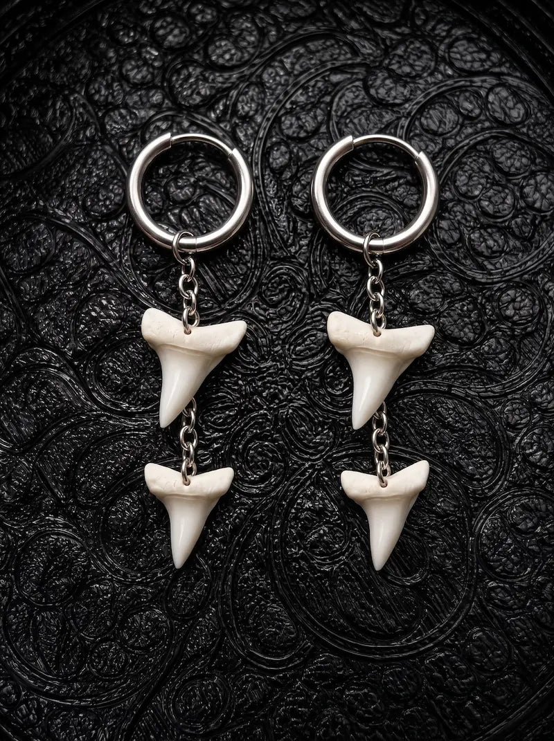 Abyss Fang shark tooth earrings with two teeth linked by chain beneath each hoop on black patterned fabric
