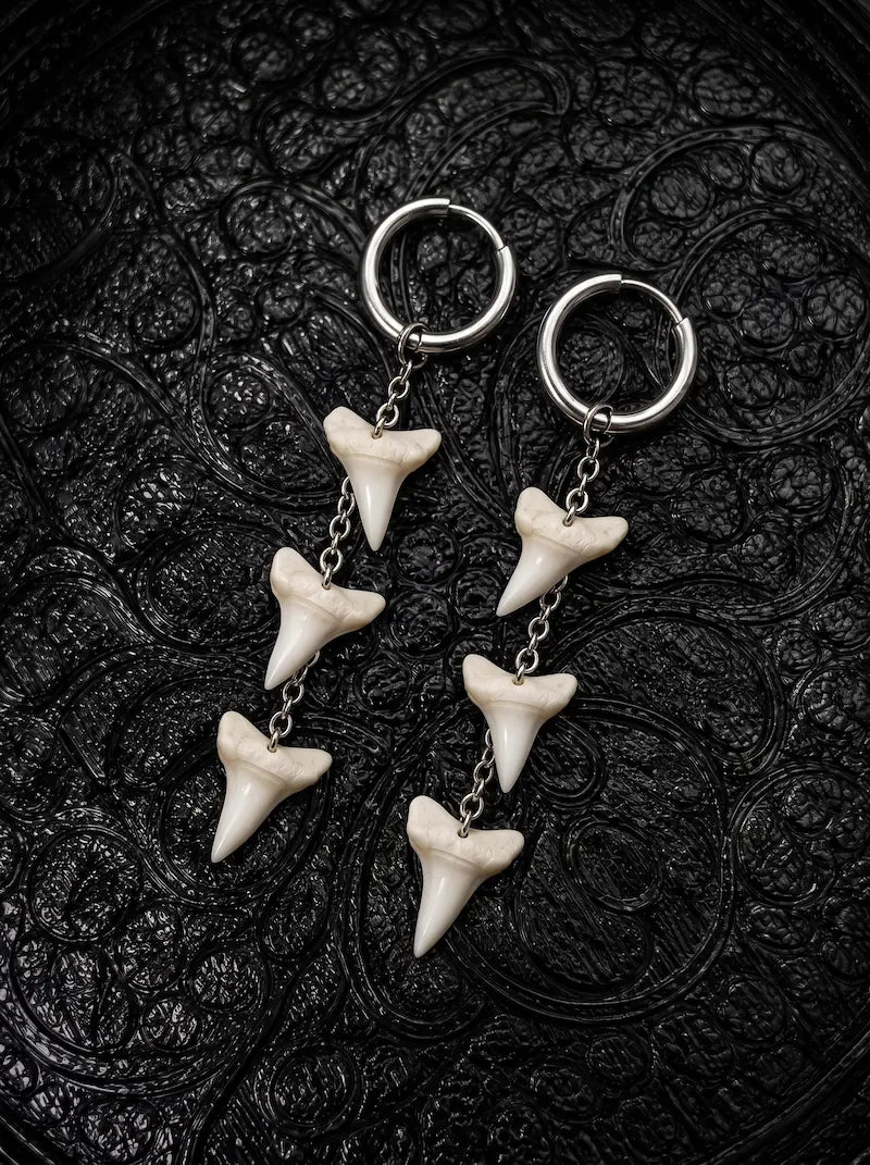 Abyss Fang shark tooth earrings with three teeth linked vertically beneath each hoop on black patterned fabric