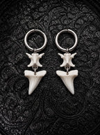 Abyssal mako shark tooth and snake bone earrings with slender pointed teeth, displayed on black patterned fabric