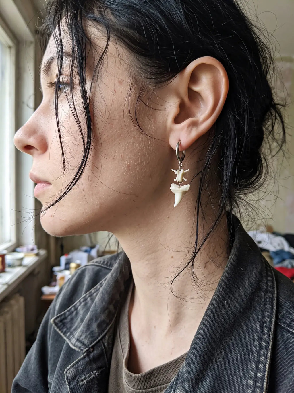 Close-up of an Abyssal earring showing a white snake vertebra and pointed shark tooth beside the neck