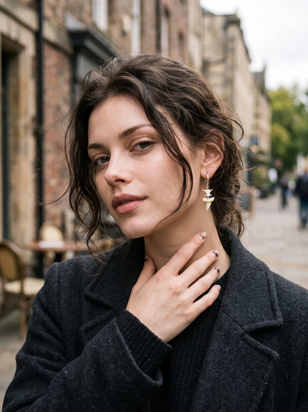 Abyssal mako shark tooth and snake bone earring worn with a dark coat and a hand at the collar