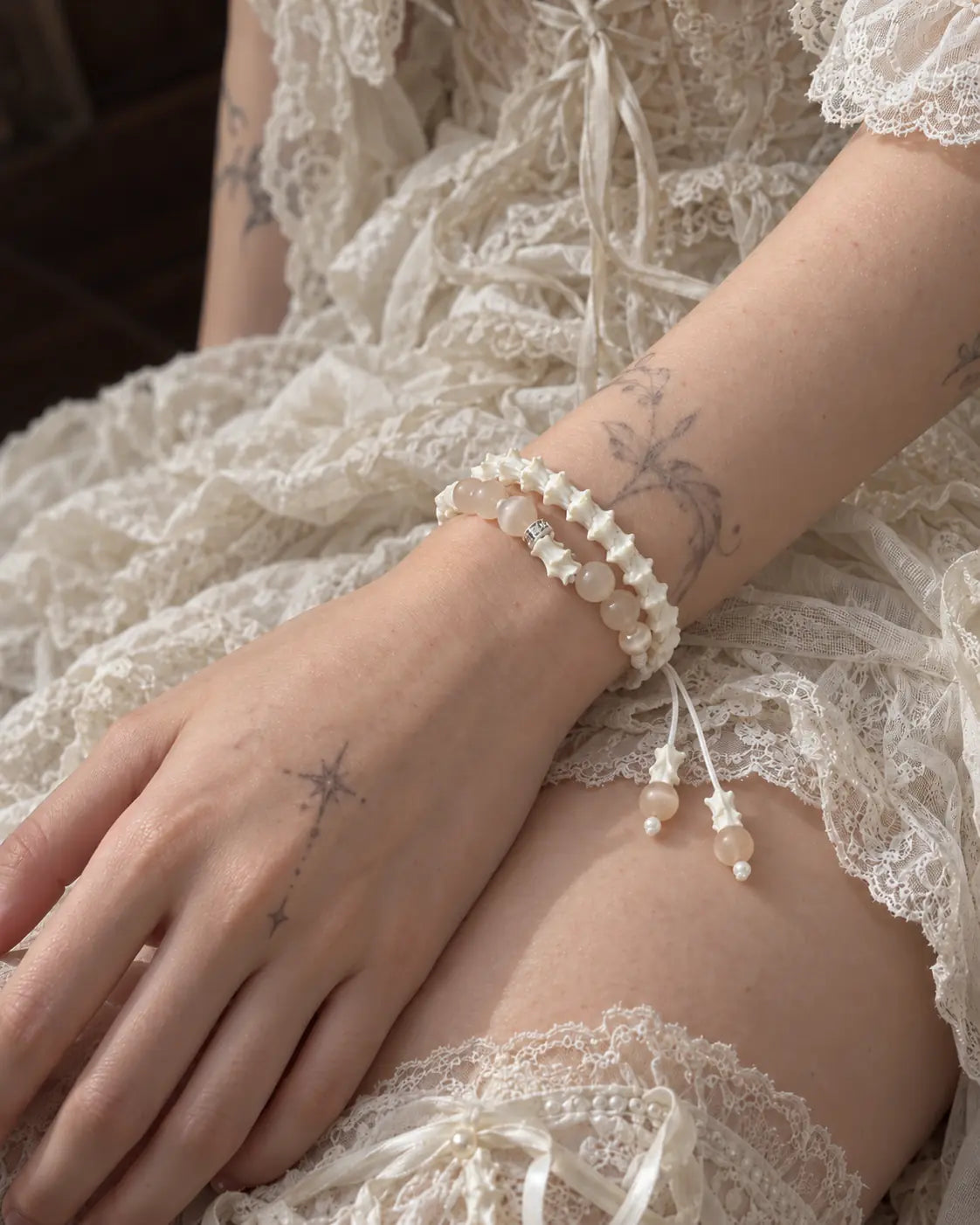 Apricot Glow snake bone bracelet on a hand resting on the thigh beside a cream lace dress