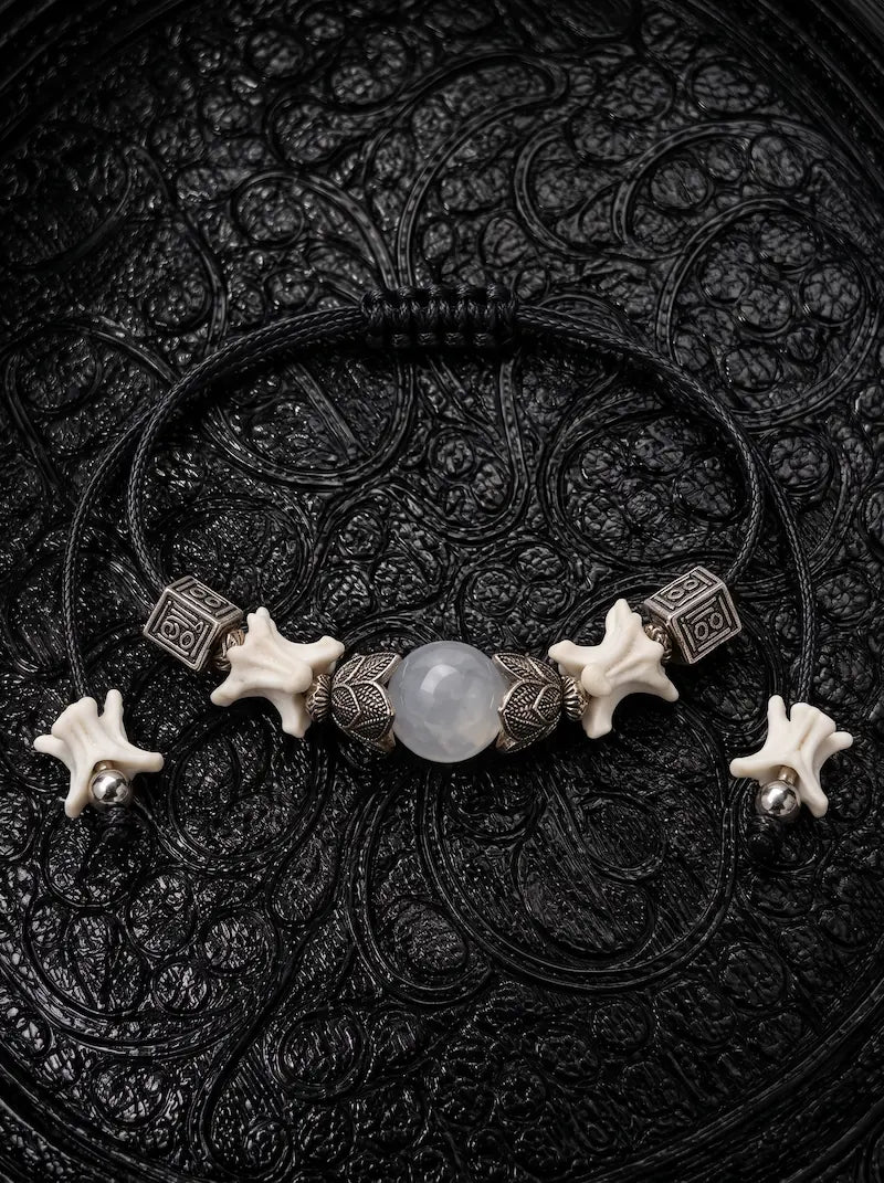 Ashen Leaf snake bone bracelet with a pale gray center bead, engraved metal accents and bone-tipped black cords