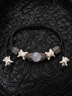 Ashen Leaf snake bone bracelet with a pale gray center bead, engraved metal accents and bone-tipped black cords