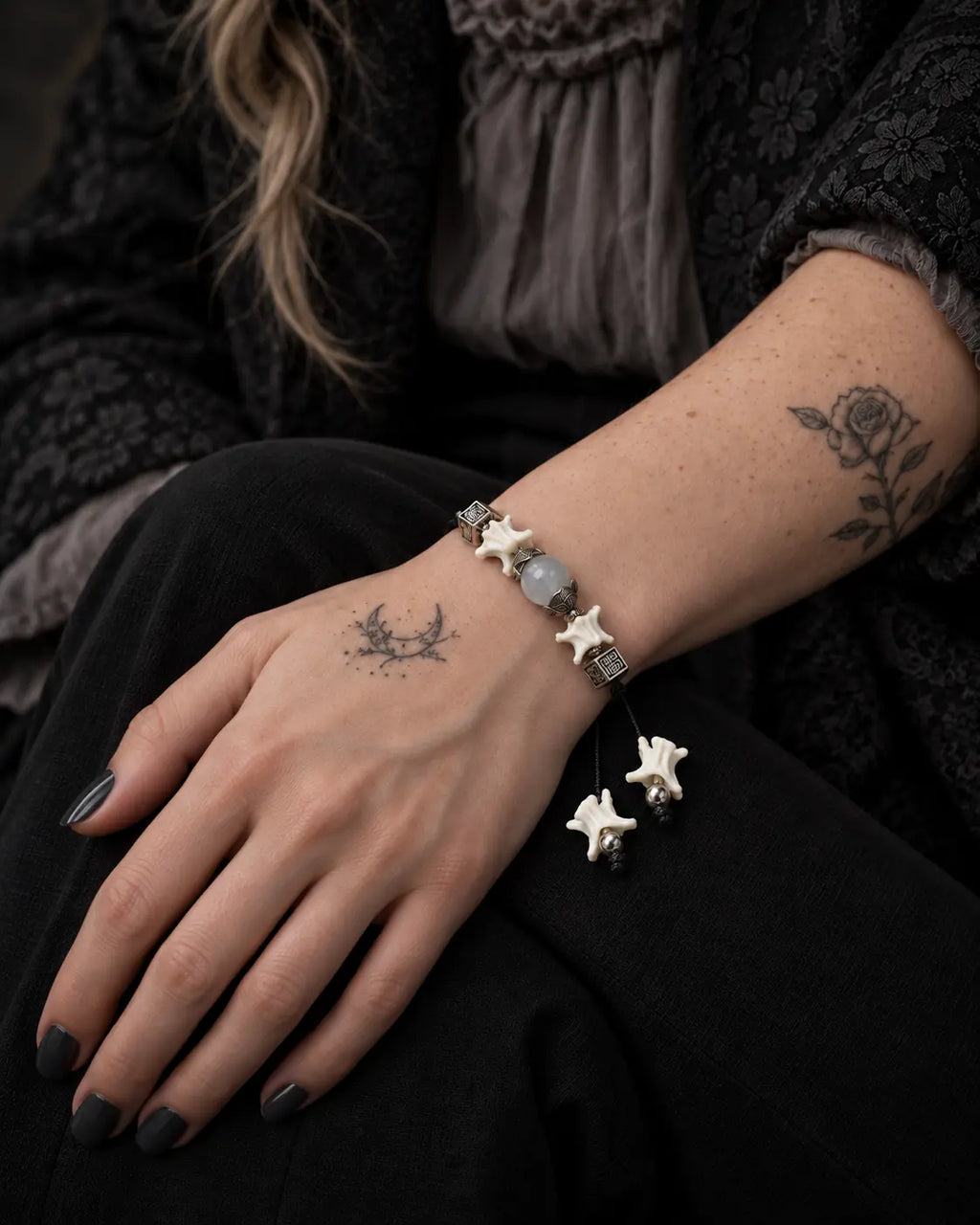 Ashen Leaf snake bone bracelet on a hand resting on the thigh, showing the gray bead and white vertebrae