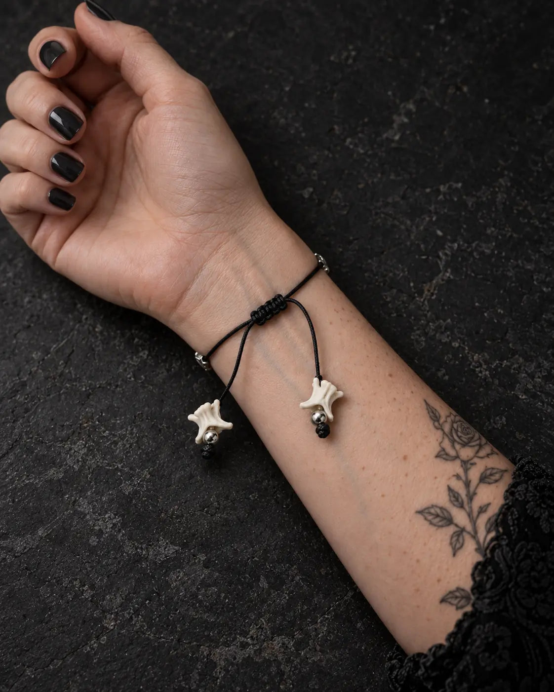Palm-up view of the Ashen Leaf snake bone bracelet showing its black sliding knot and two bone-tipped cords