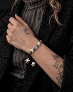 Ashen Leaf snake bone bracelet shown on a raised wrist beside a gray blouse and black jacket