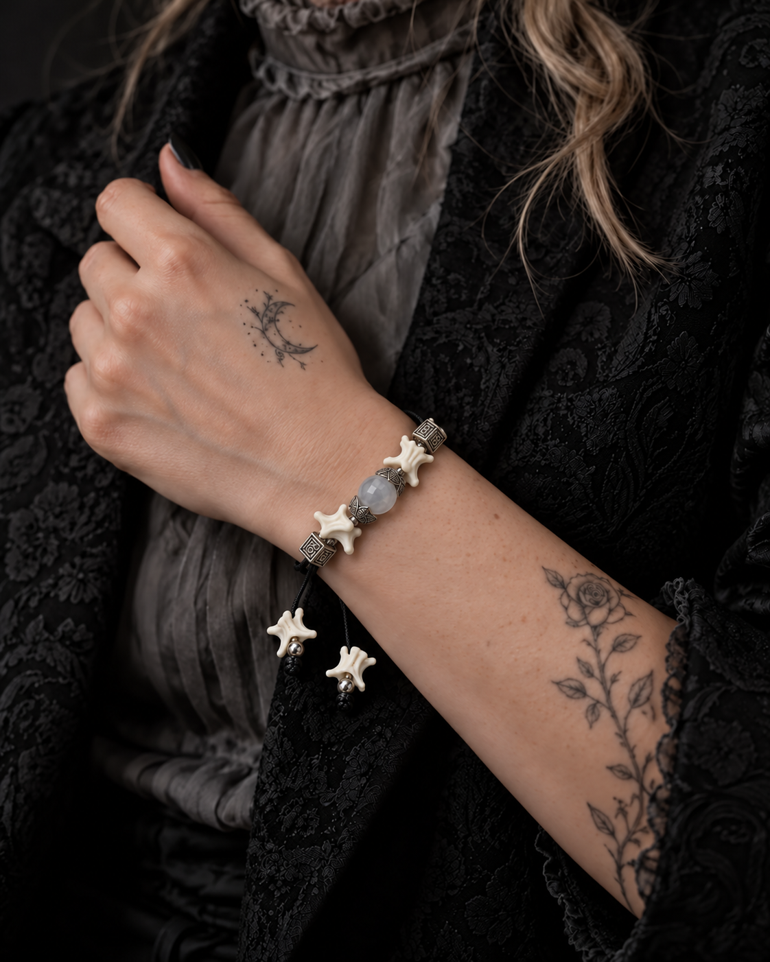 Ashen Leaf snake bone bracelet shown on a raised wrist beside a gray blouse and black jacket