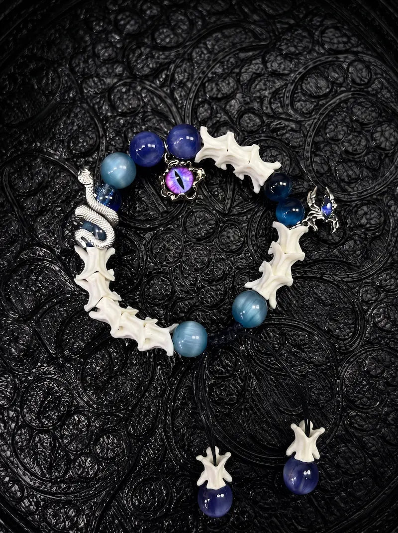 Azure Serpent Eye snake bone bracelet with blue beads, a silver-tone serpent and an iridescent eye charm on black fabric