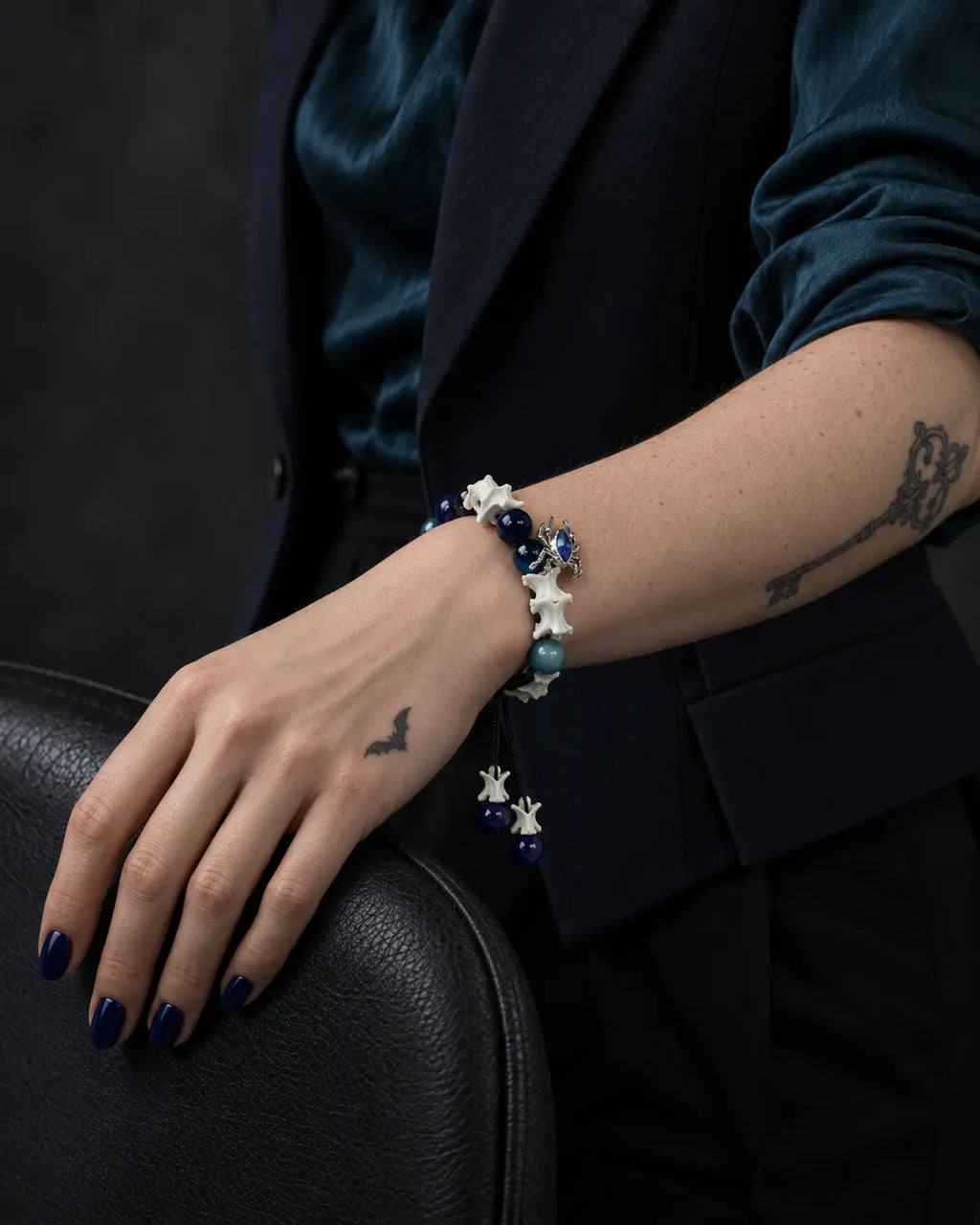 Azure Serpent Eye snake bone bracelet on a wrist resting over the curved back of a dark chair