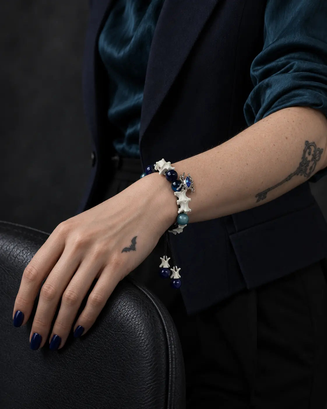 Azure Serpent Eye snake bone bracelet on a wrist resting over the curved back of a dark chair