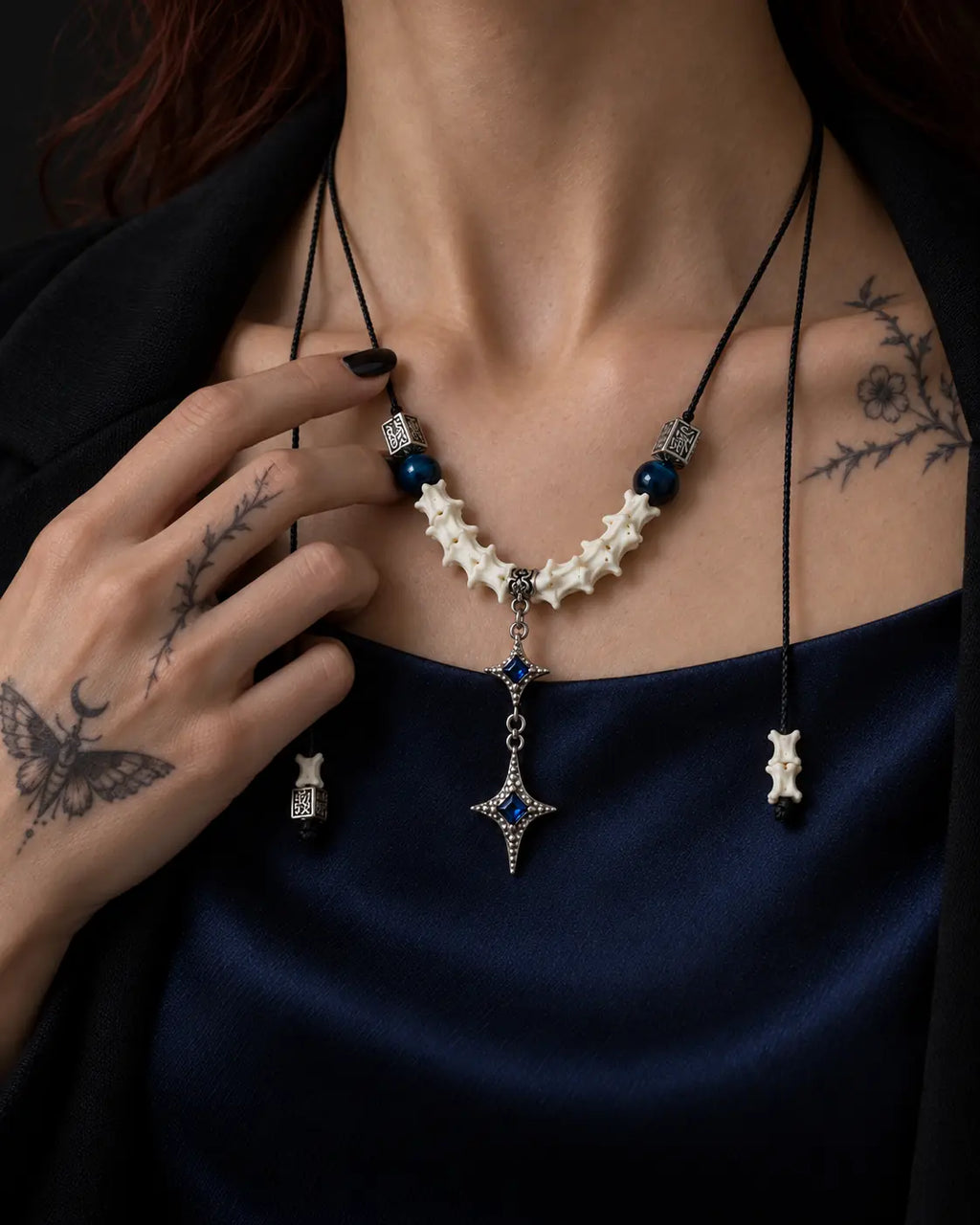 Azure Twin Star snake bone necklace worn above a blue satin neckline with a hand beside the blue beads