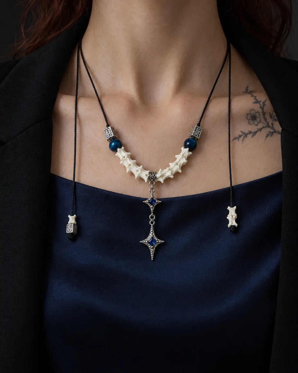 Front view of the Azure Twin Star snake bone necklace over blue satin, with its cord ends hanging at each side