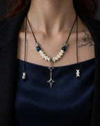 Front view of the Azure Twin Star snake bone necklace over blue satin, with its cord ends hanging at each side
