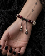 Palm-up view of the Bagua Coin snake bone bracelet showing its black sliding knot, red beads and cube-tipped cords