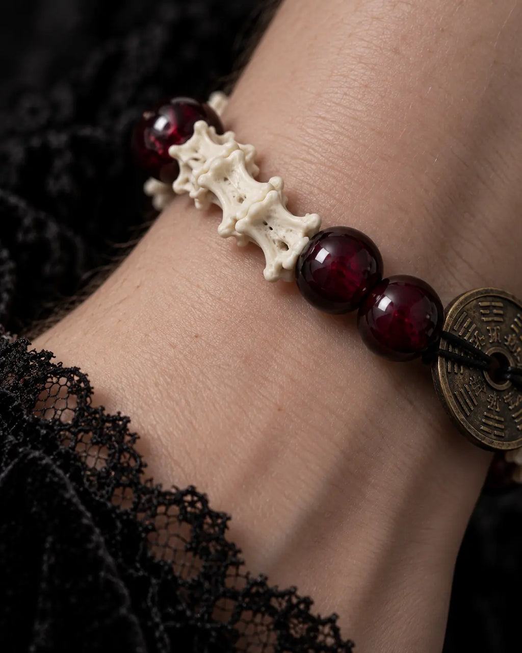 Macro view of the Bagua Coin snake bone bracelet showing white vertebrae and deep red beads beside the engraved coin