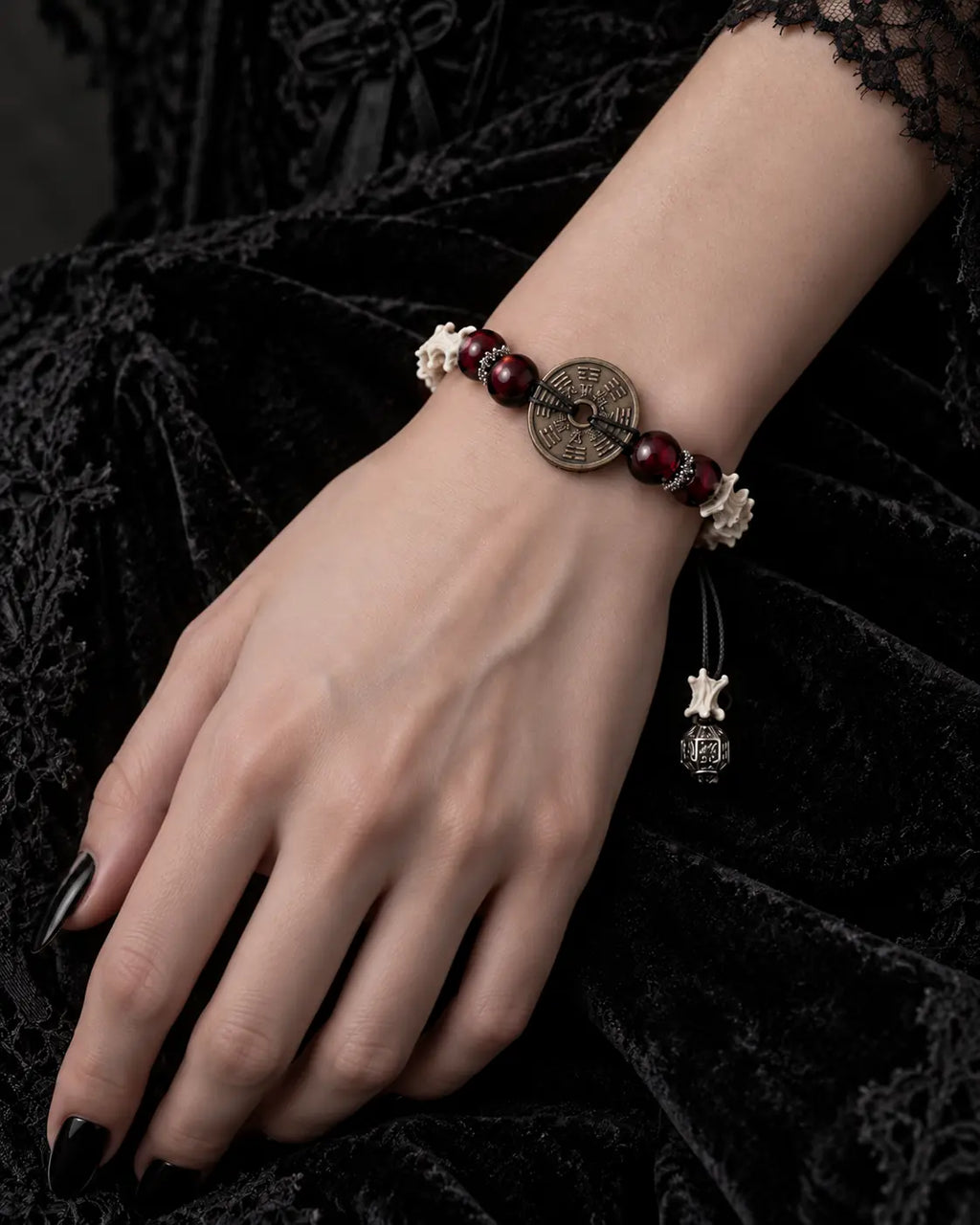Bagua Coin snake bone bracelet on a hand resting on black velvet, with its round engraved coin facing upward