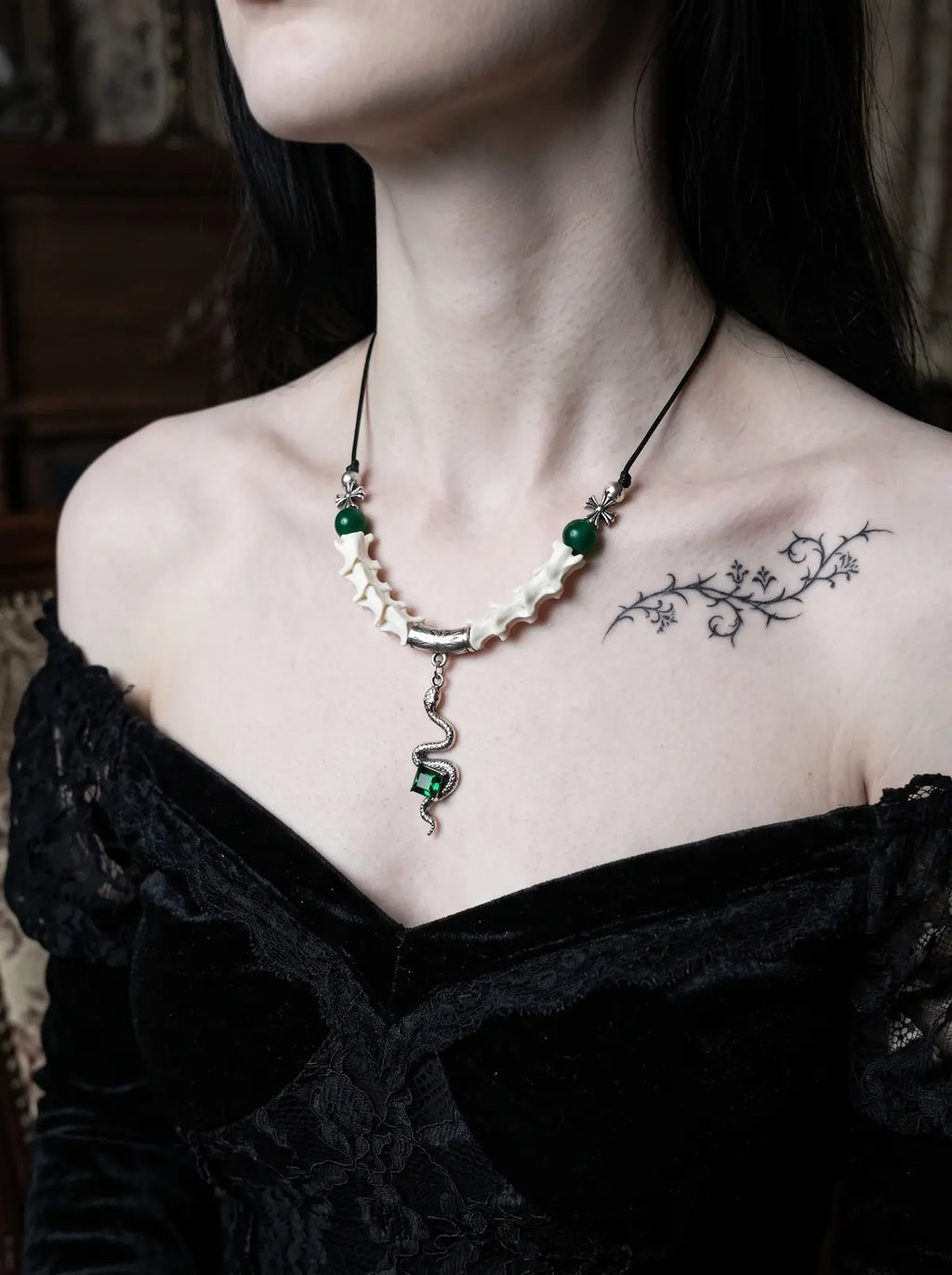 Basilisk Jewel Snake Bone Necklace, pale snake bone necklace with small green accents over a black off-shoulder top