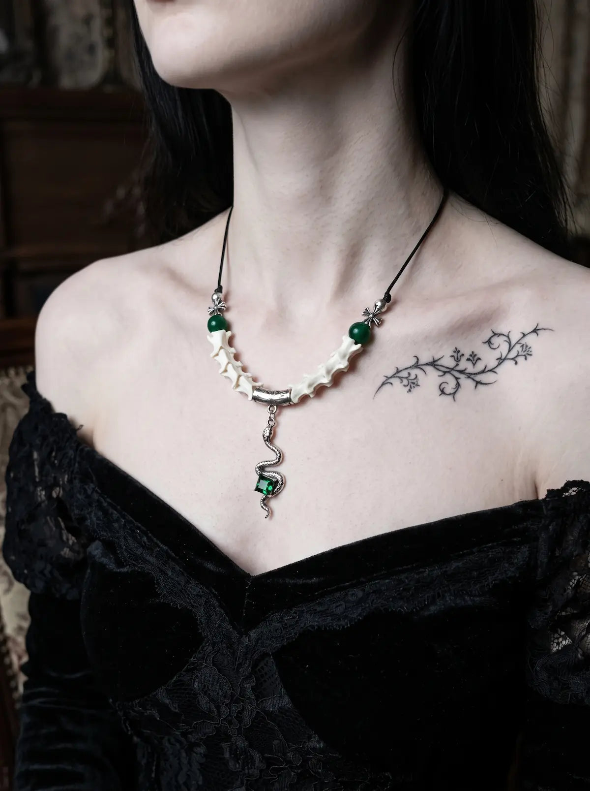 Basilisk Jewel Snake Bone Necklace, pale snake bone necklace with small green accents over a black off-shoulder top