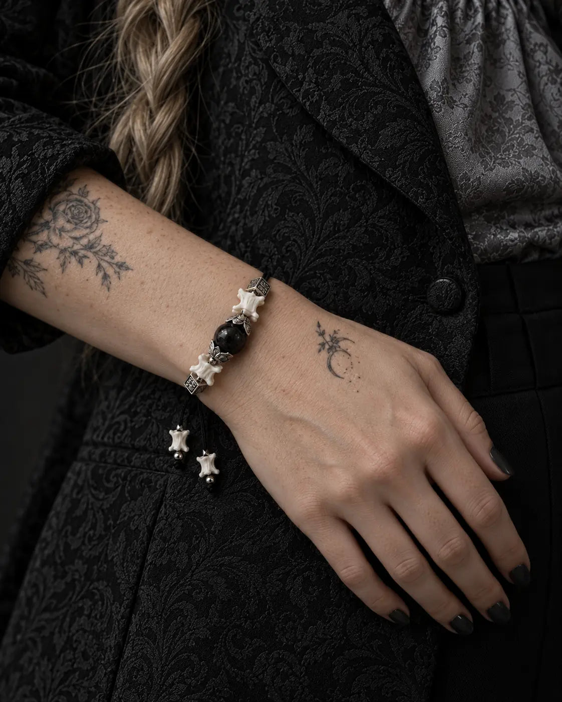 Black Orb snake bone bracelet worn with the hand resting across the waist of a black patterned jacket