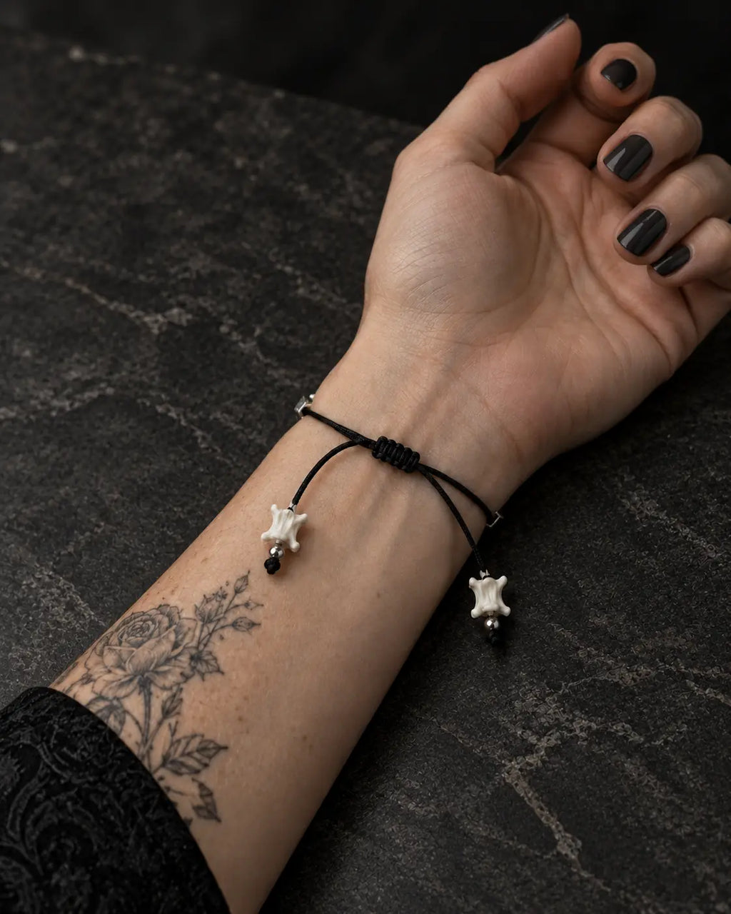 Palm-up view of the Black Orb snake bone bracelet showing its sliding knot and two bone-tipped black cords