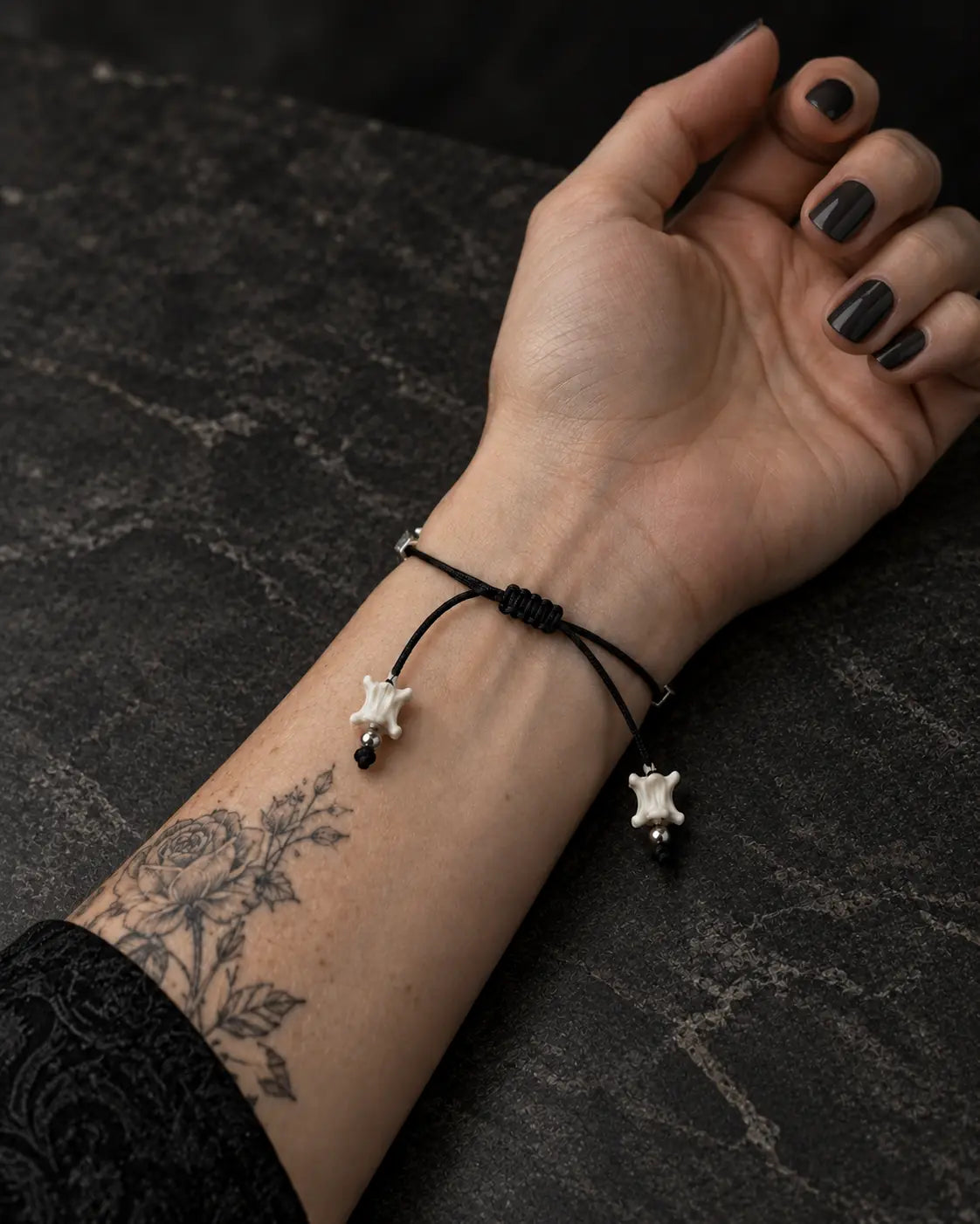 Palm-up view of the Black Orb snake bone bracelet showing its sliding knot and two bone-tipped black cords