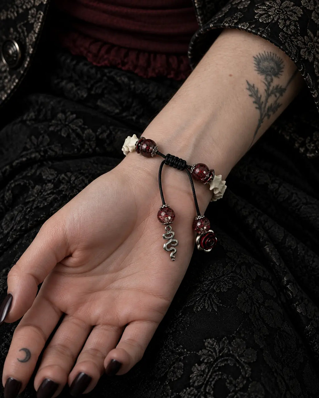 Palm-up view of the Blood Dragon snake bone bracelet showing its black sliding knot and dangling serpent and rose charms