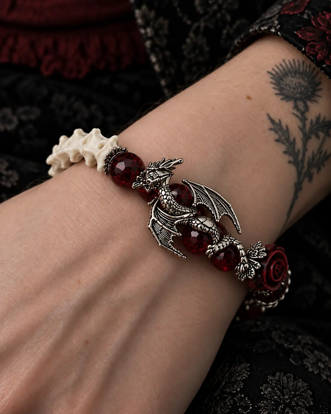 Blood Dragon snake bone bracelet detail showing a winged dragon, crimson beads and a dark rose beside white vertebrae