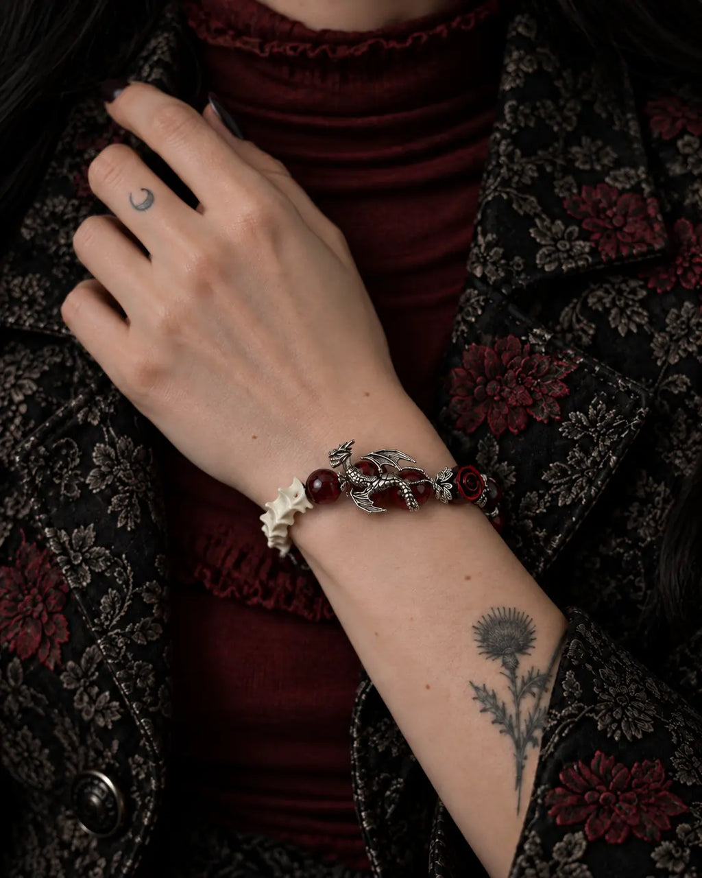Blood Dragon snake bone bracelet worn with the hand at the lapel of a floral jacket over burgundy clothing