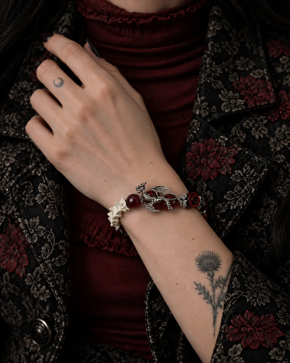 Blood Dragon snake bone bracelet worn with the hand at the lapel of a floral jacket over burgundy clothing