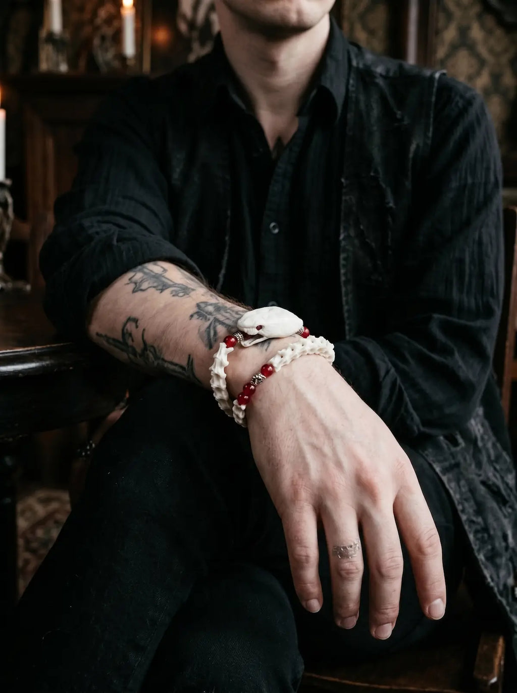 Bloodlance Snake Bone Bracelet, red and white snake bone bracelet worn on an exposed forearm, seated pose