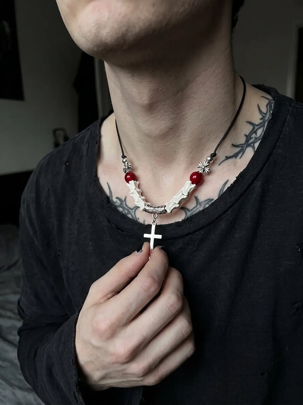 Bloodmark Cross Snake Bone Necklace, close view of pale vertebrae and dangling cross held by a model wearing black