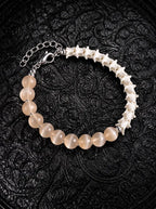 Blush Arc snake bone bracelet with peach beads, white vertebrae and a silver-tone chain clasp on black patterned fabric