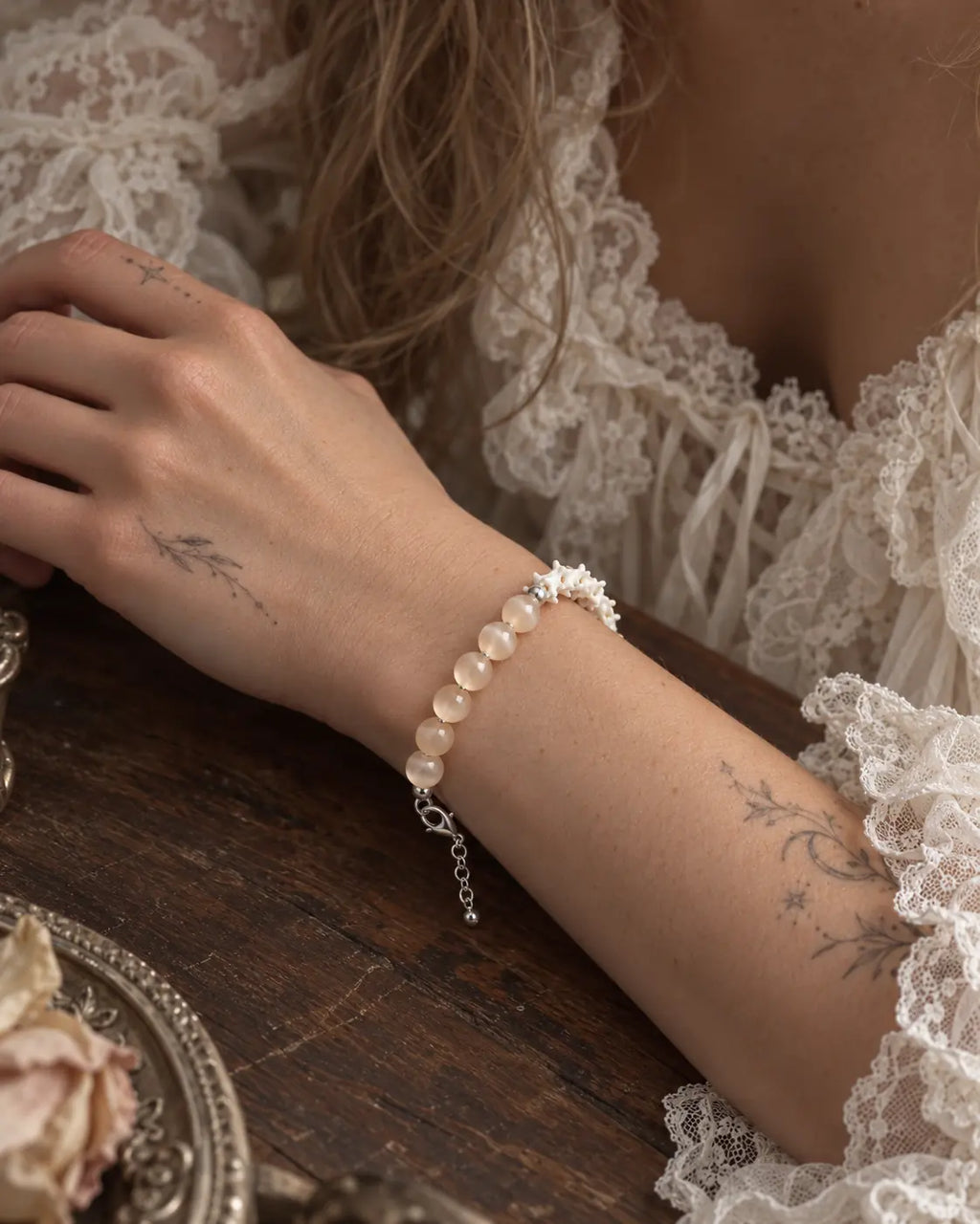 Blush Arc snake bone bracelet on a wrist resting on a wooden table, with its extension chain hanging below