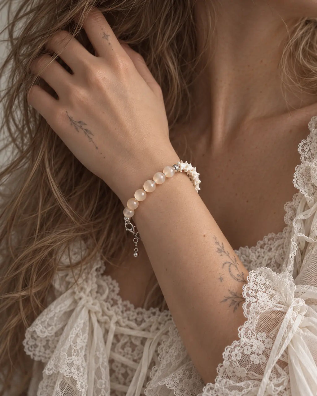 Close-up of the Blush Arc snake bone bracelet showing peach beads and white vertebrae as the hand touches the hair