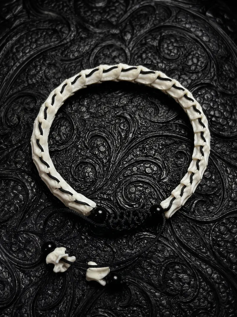 Bonebound Snake Bone Bracelet, pale snake vertebrae arranged in a circle with black cord closure on black fabric