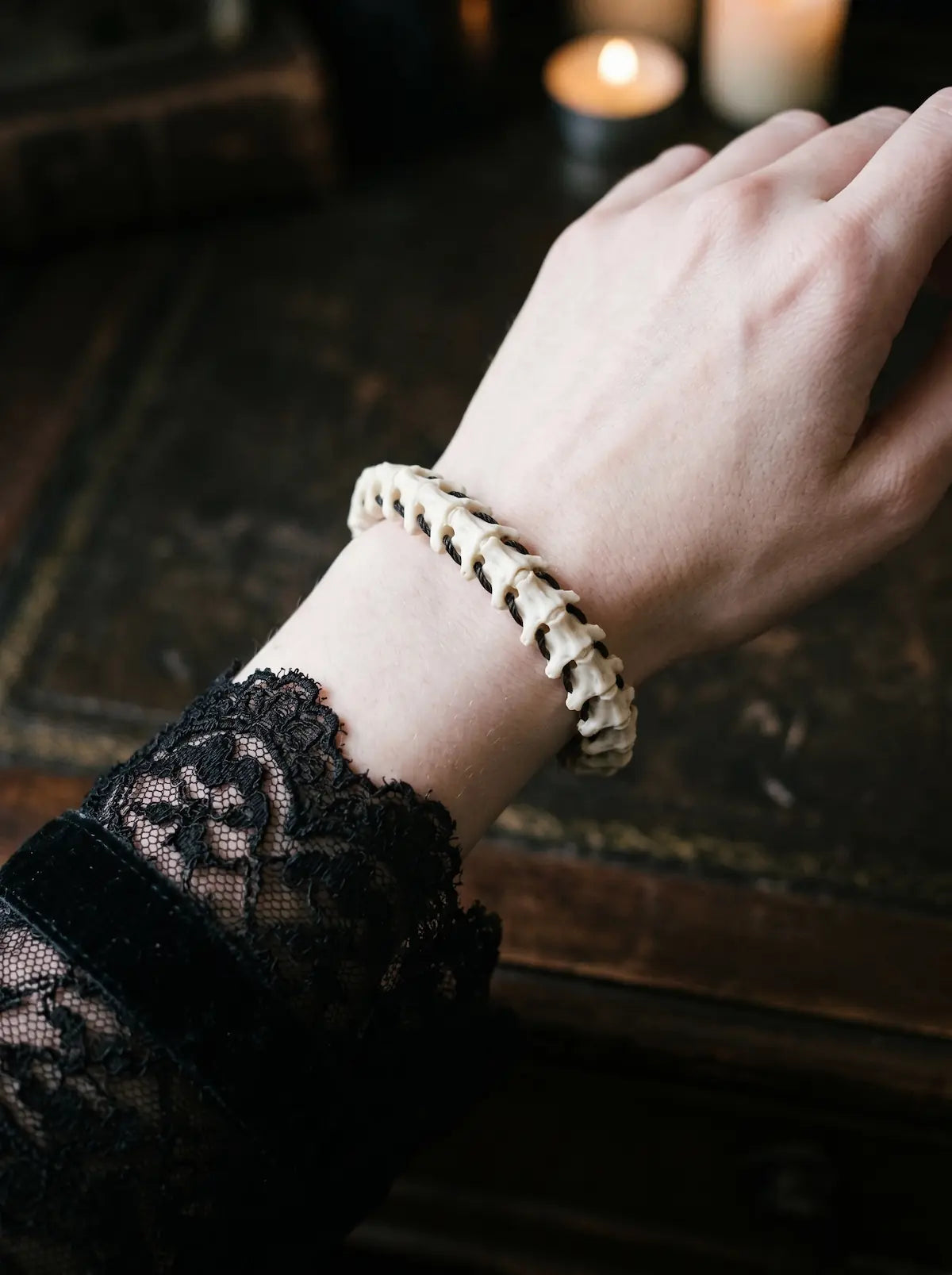 Bonebound Snake Bone Bracelet, pale vertebrae bracelet worn snugly on the wrist above a black lace sleeve