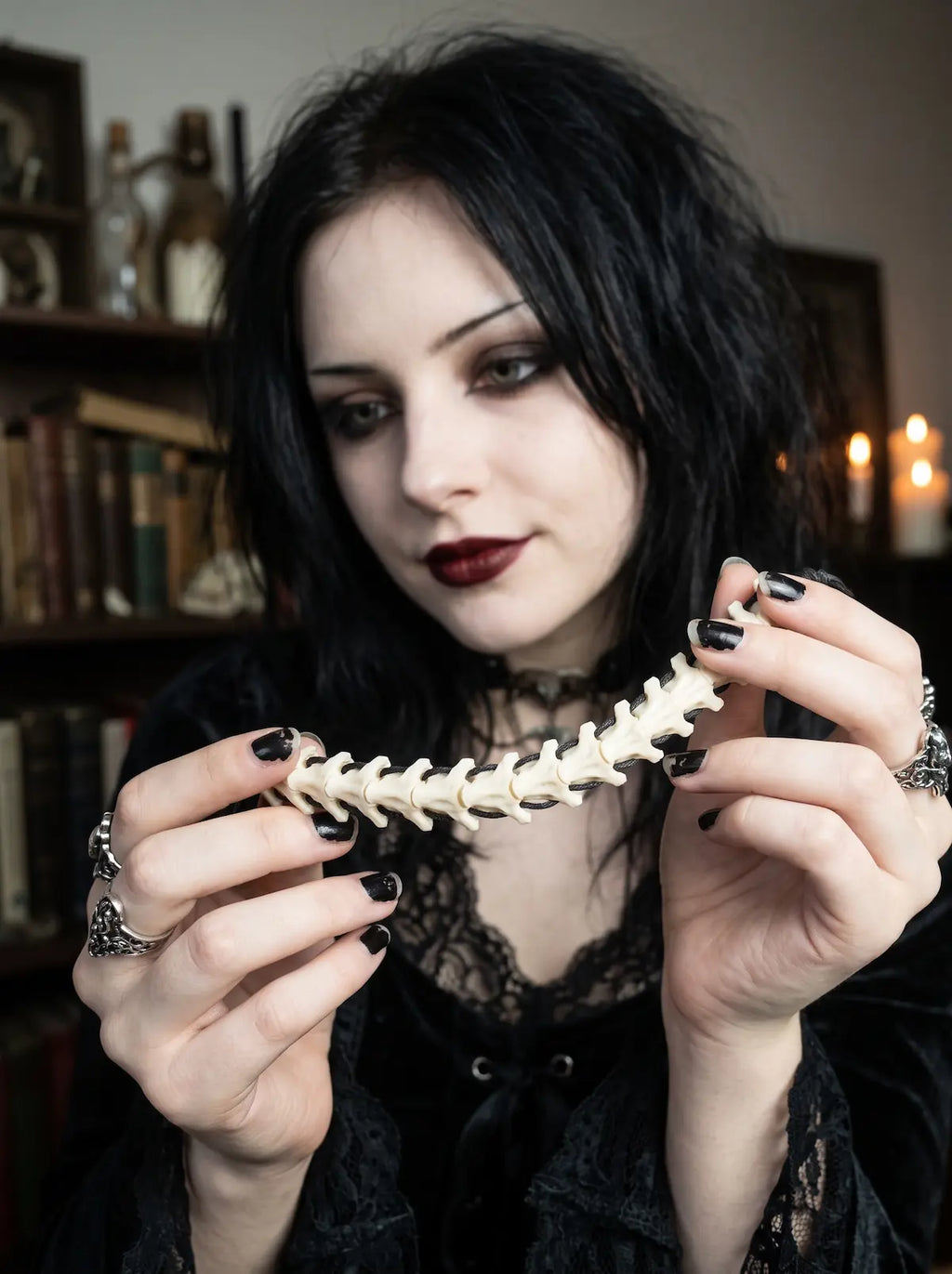 Bonebound Snake Bone Bracelet, model holding the pale snake bone bracelet near the face in a dark interior