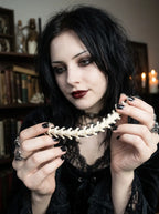 Bonebound Snake Bone Bracelet, model holding the pale snake bone bracelet near the face in a dark interior