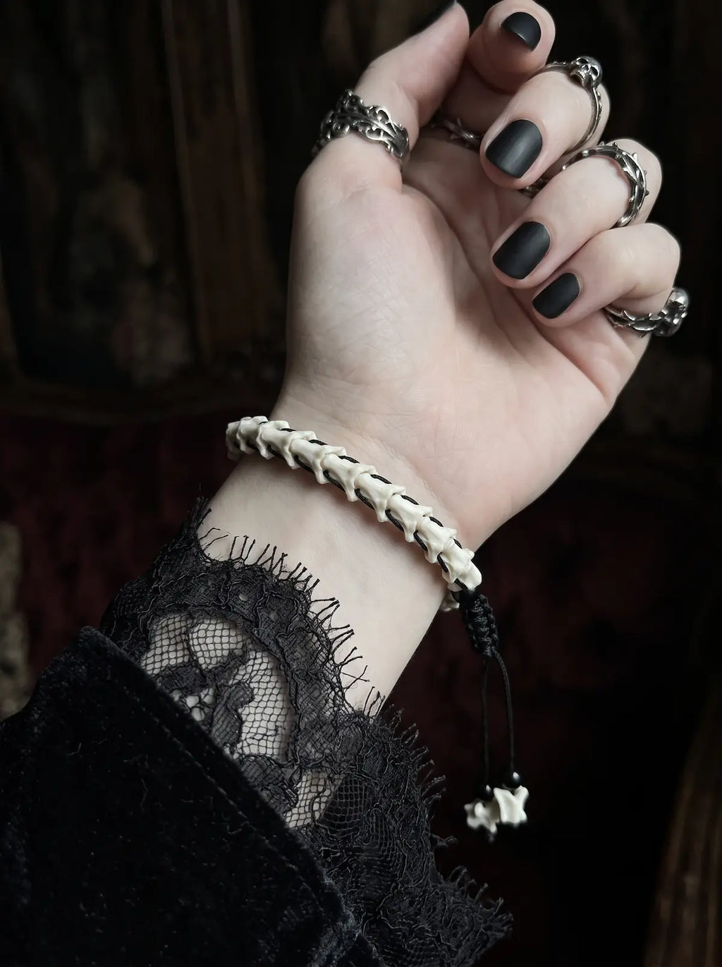 Bonebound Snake Bone Bracelet, bone bracelet on a raised wrist showing its dangling black cords and charms