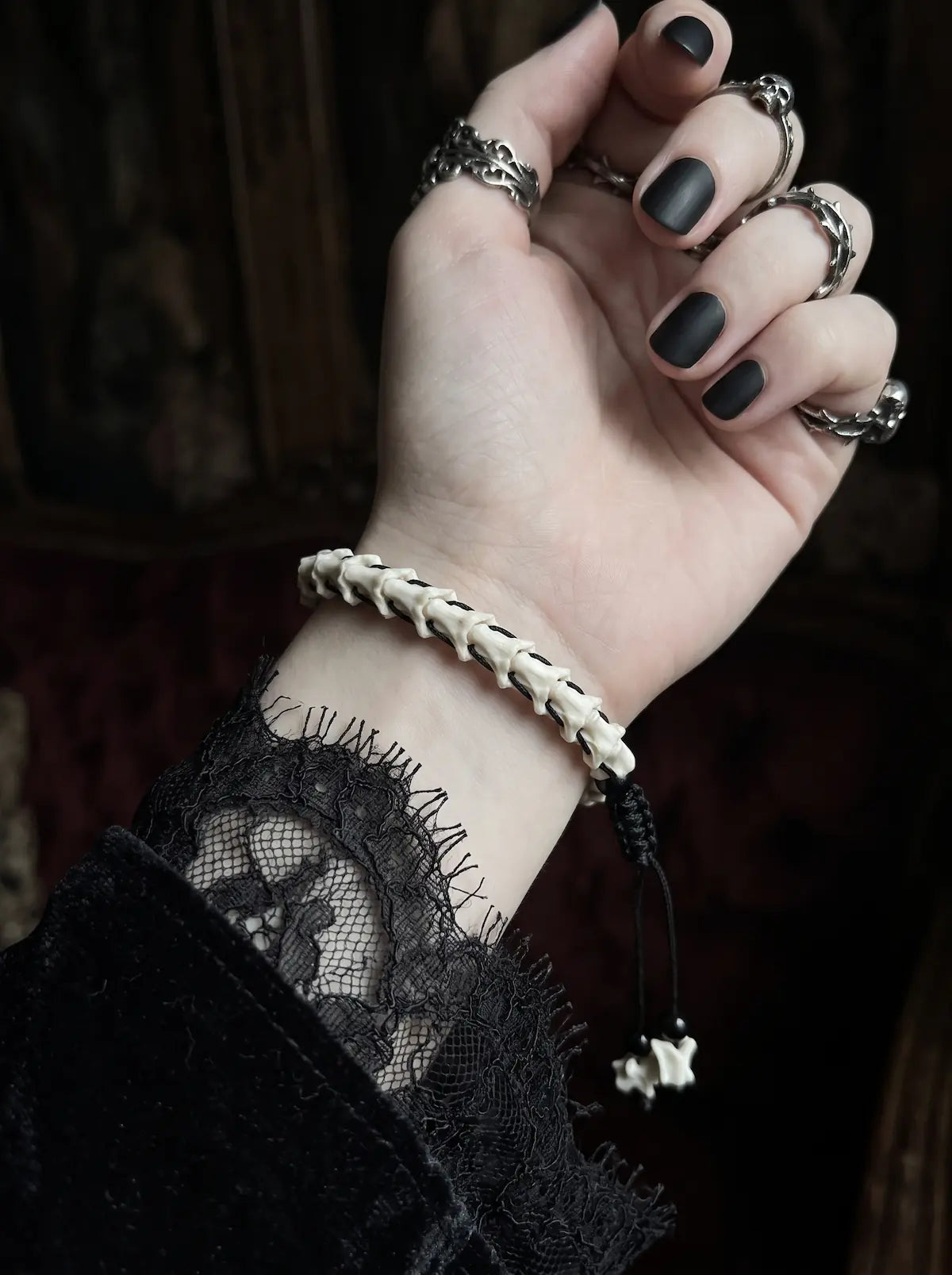Bonebound Snake Bone Bracelet, bone bracelet on a raised wrist showing its dangling black cords and charms