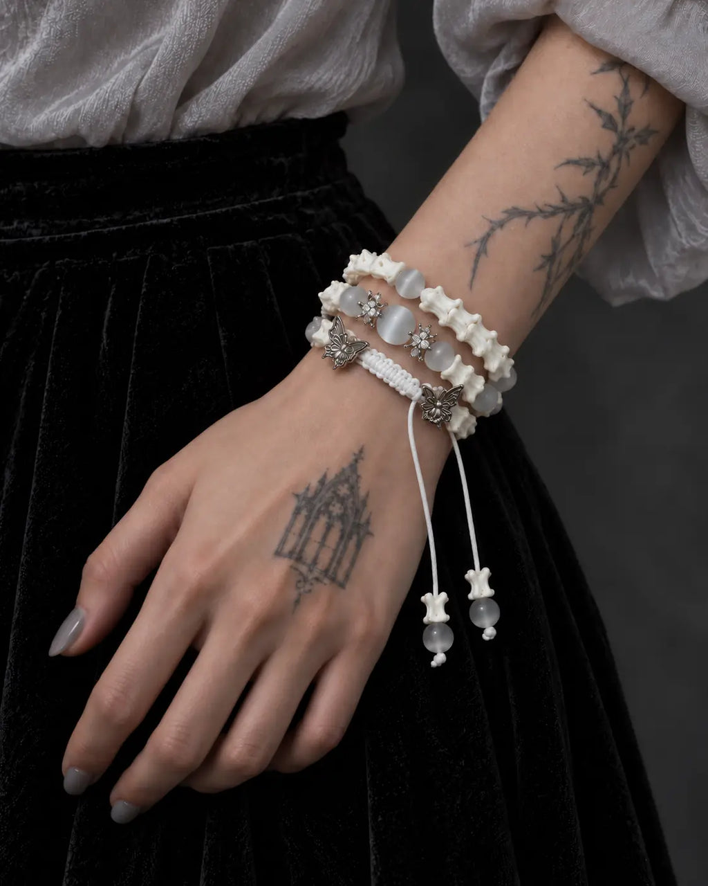 Angled view of the Butterfly Mist snake bone bracelet and dangling gray beads beside a pale gray sleeve
