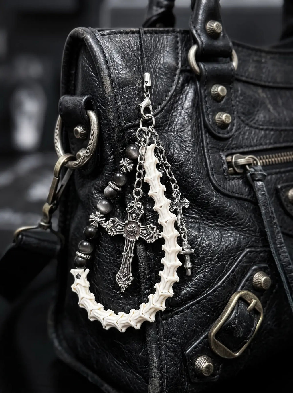 Cathedral Relic Snake Bone Keychain, snake bone keychain with dangling metal charms attached to a black leather bag