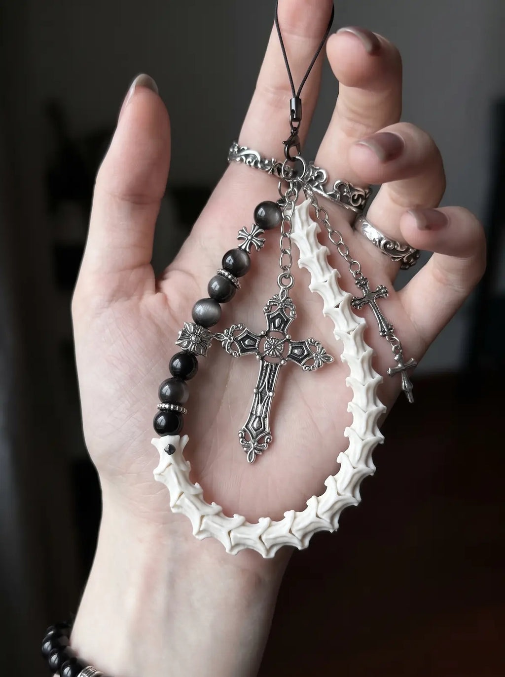 Cathedral Relic Snake Bone Keychain, close view of a white vertebrae loop and cross pendants on dark bag hardware