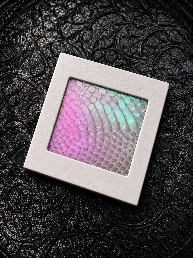 Chromatic Relic snakeskin bookmark charm with pink and pale green scales in a white frame on black patterned fabric