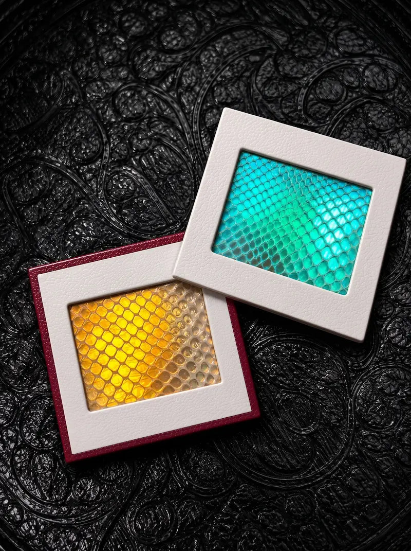 Turquoise and golden yellow Chromatic Relic snakeskin bookmark charms in overlapping square frames on black fabric