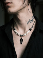 Coffin Oath Snake Bone Necklace, pale vertebrae necklace with black beads and coffin charm above a dark shirt