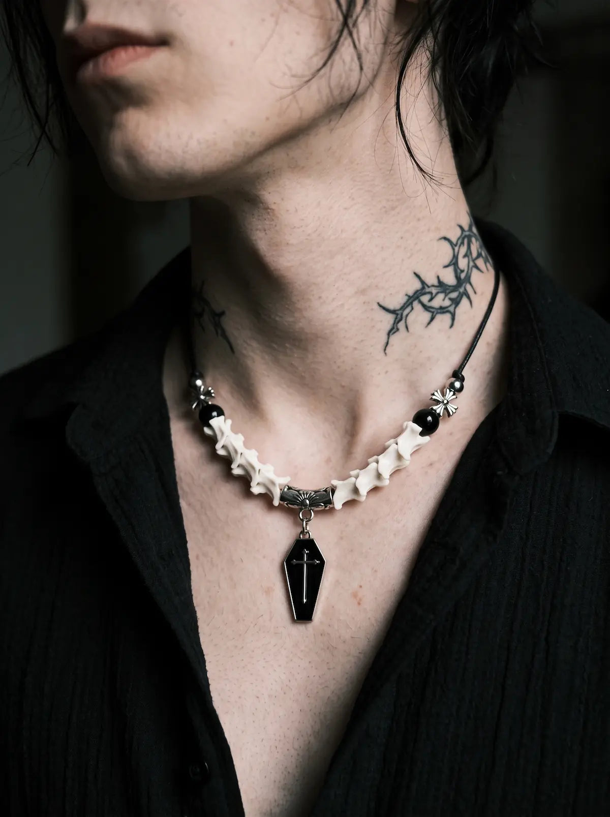 Coffin Oath Snake Bone Necklace, pale vertebrae necklace with black beads and coffin charm above a dark shirt